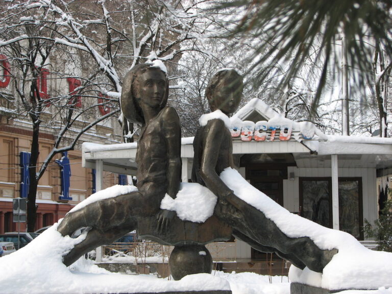Уличная скульптура Пети и Гаврика в Одессе зимой на фоне городской улицы.